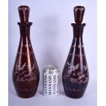 A PAIR OF EARLY 20TH CENTURY BOHEMIAN RUBY GLASS DECANTERS AND STOPPERS decorated with deer and land