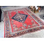 A large Middle Eastern red ground carpet decorated with a blue lozenge of flowers. 354 cm x 264 cm