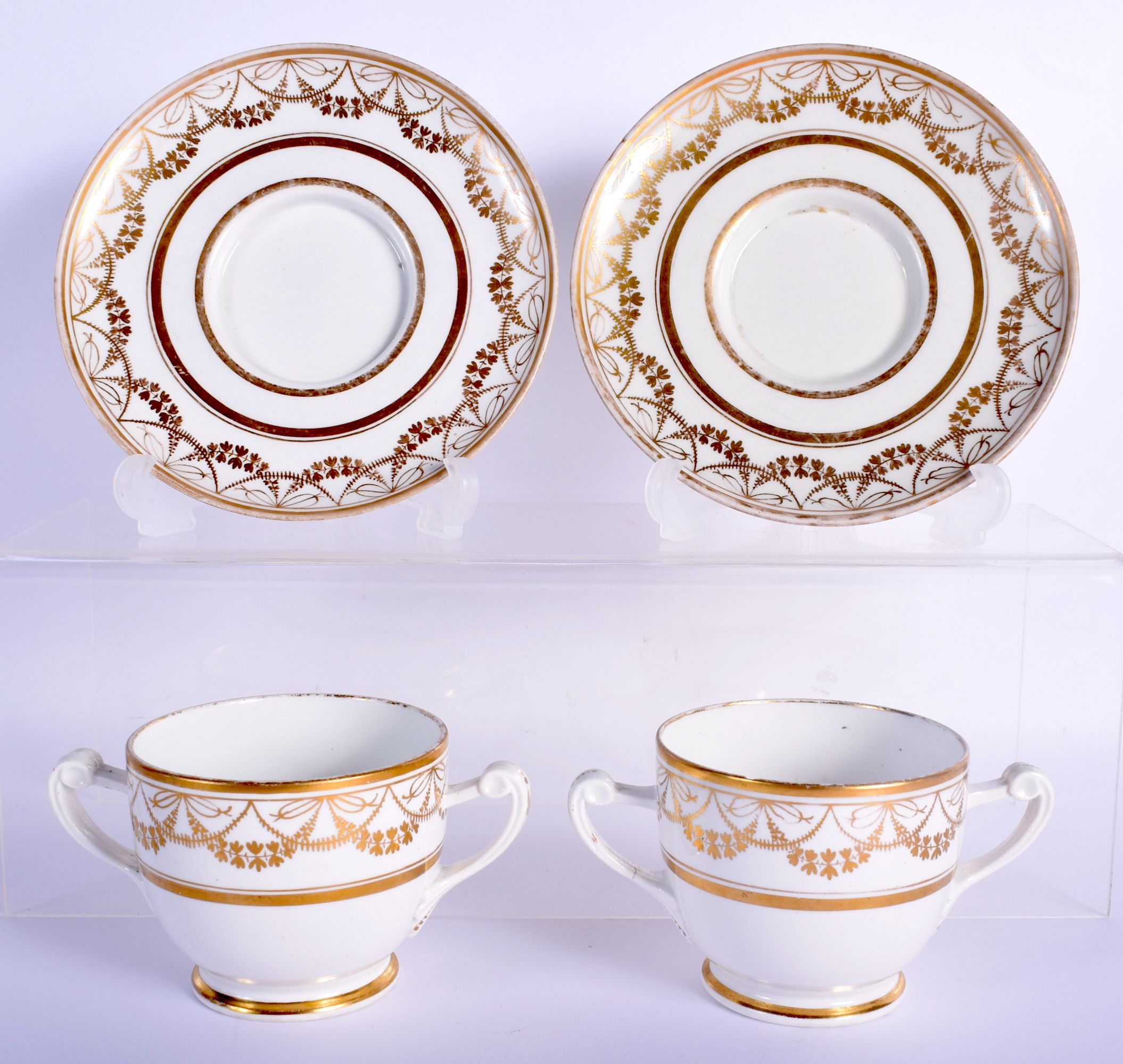 A PAIR OF EARLY 19TH CENTURY TWIN HANDLED GILDED CUPS AND SAUCERS Coalport or Derby, painted with ne