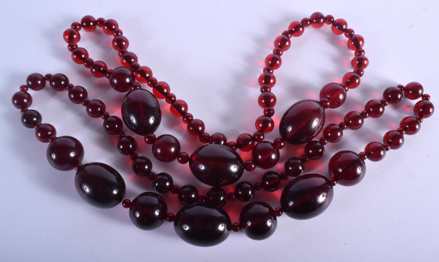 A PAIR OF ART DECO CHERRY AMBER TYPE NECKLACES. 260 grams. 68 cm long, largest bead 4.5 cm x 2.75 cm