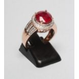 A DRESS RING, the round facet cut red gemstone claw set to a border of pave set small diamonds to
