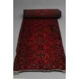 A PERSIAN RUNNER, modern, the burgundy field with ten square panels each centred by a floral gul,