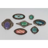 A COLLECTION OF SEVEN RUSKIN TYPE ARTS AND CRAFTS PEWTER BROOCHES, each inset with a coloured