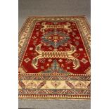 A CAUCASIAN STYLE RUG, modern, the red field with flowerheads and central pale blue gul, ivory