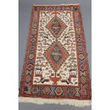 A PERSIAN TRIBAL RUG, the ivory field with two linked brick red guls, the whole featuring various