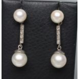 A PAIR OF CULTURED PEARL DROP STUD EARRINGS, the two graduated white pearls tied by a bar pave set