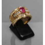 A RUBY AND DIAMOND COCKTAIL RING, the central oval facet cut ruby claw set to borders channel and