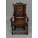 A JOINED OAK ARMCHAIR, c.1700, the panelled back carved with tulips and dated "1694" below and a