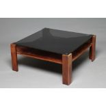 A ROSEWOOD VENEERED COFFEE TABLE, 1970s, of square X form with inset smoke glass top, raised on four