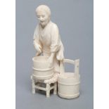 A JAPANESE IVORY FIGURE, Meiji period, carved as an old lady standing barefoot beside two pails,