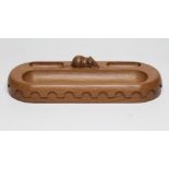 A ROBERT THOMPSON OAK DESK STAND, modern, of plain D end form with deep long pen tray, carved