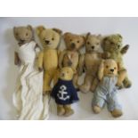 A collection of seven vintage teddy bears, including one in a long white skirt and a one with a