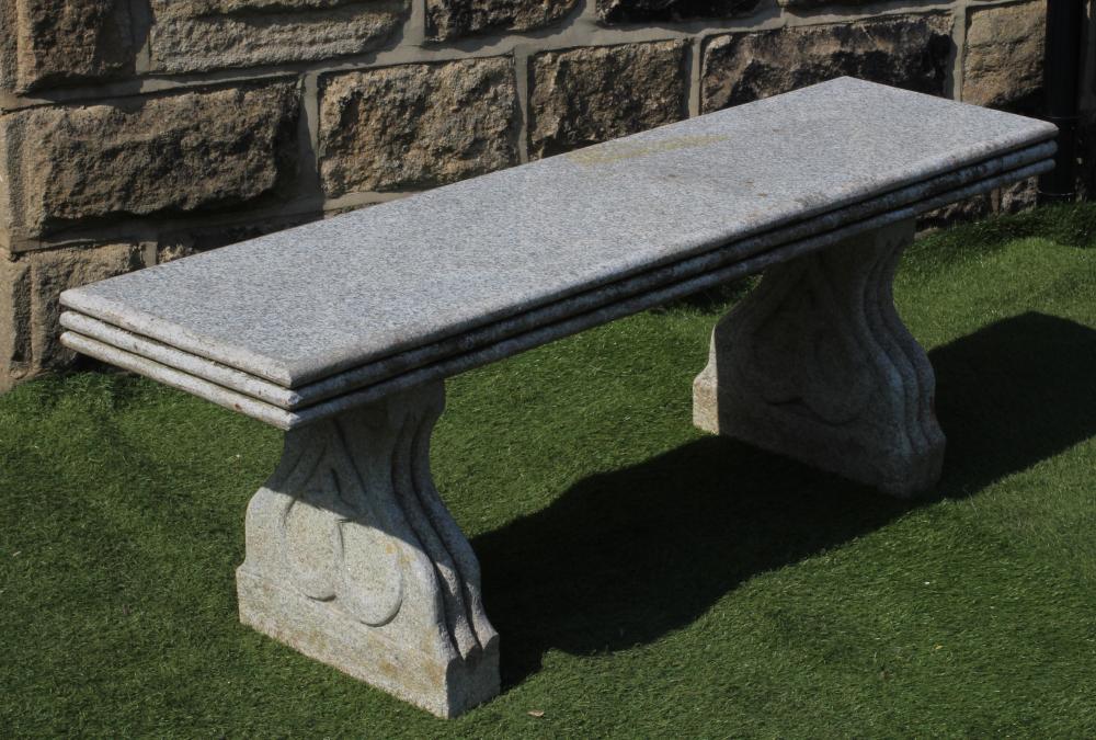 A GRANITE BENCH, the moulded edged oblong seat on shaped end supports each with a heart motif,