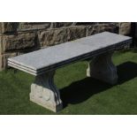 A GRANITE BENCH, the moulded edged oblong seat on shaped end supports each with a heart motif,