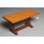 A ROBERT THOMPSON ADZED OAK COFFEE TABLE, the rounded oblong top on turned and faceted end supports,