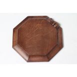 A ROBERT THOMPSON ADZED OAK TEAPOT STAND/CHOPPING BOARD of octagonal form, the dished sides with