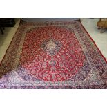 A PERSIAN STYLE WOOL CARPET, the bright red field with trailing flower centred by a navy blue and