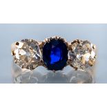 A SAPPHIRE AND DIAMOND THREE STONE RING, the central oval facet cut sapphire claw set and flanked by