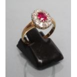 A RUBY AND DIAMOND CLUSTER RING, the oval facet cut ruby claw set to a border of ten round