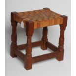 A ROBERT THOMPSON OAK STOOL of oblong form with lattice leather seat, raised on faceted baluster