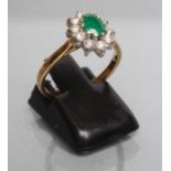 AN EMERALD AND DIAMOND CLUSTER RING, the oval facet cut emerald claw set to a border of ten small