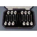 A SET OF TWELVE SEAL TOP SILVER TEASPOONS, maker's mark CB & S, Sheffield 1924, with matching tongs,