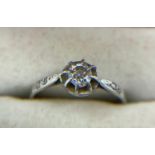 A solitaire diamond ring with tiny diamonds to the shoulders set in unmarked white metal. Size O.