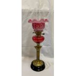 A 19thC cranberry glass oil lamp with cranberry and white glass shade, Corinthian brass column and