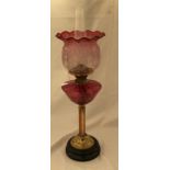 A Victorian cranberry glass oil lamp with brass column and slate base and an acid etched cranberry