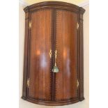 A 19thC bow fronted oak hanging corner cupboard. Brass H hinges and inlay to doors. 96 h x 40cms d.