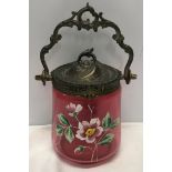 A Victorian cranberry glass biscuit barrel with painted floral design and brass spelter top and