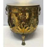 A large brass circular log bucket with embossed decoration, lion head handles, tripod claw feet