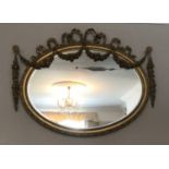 A decorative gilt and gesso framed 19thC oval bevel edged wall mirror. Frame surmounted with bow and