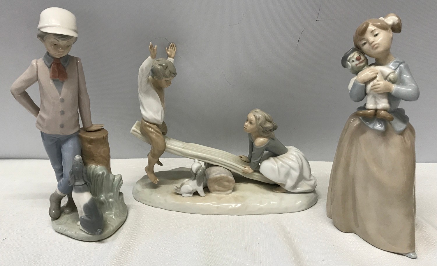 Three Nao Lladro figurines : Girl with Clown Doll 22.5cms h, Boy with Dog 23cms h and Boy and Girl