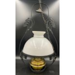 A brass and iron hanging oil lamp with floral decoration to iron work and a glass white shade.