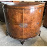 A walnut veneered half round side cabinet with decorative brass fittings, shelved interior and