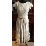 A Traina Norell of New York cream linen 1950's dress with gathered shirt to waist and belt, applique
