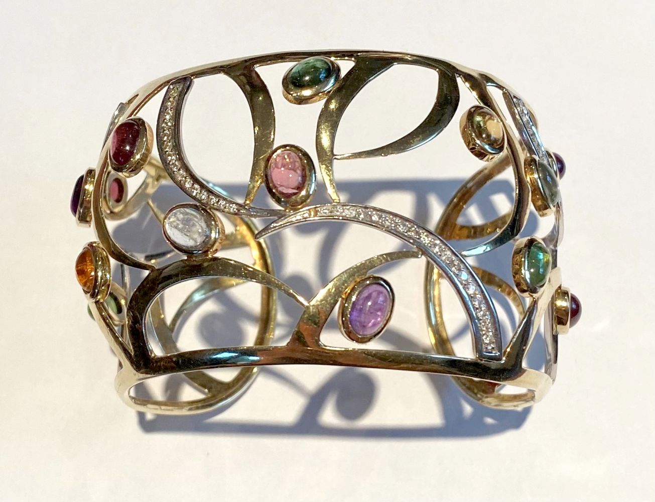 A 14CT YELLOW GOLD OPEN WORK CONTEMPORARY DESIGN BANGLE, mounted with 15 cabochon amethyst,