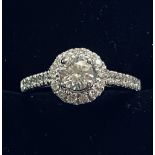 AN 18CT WHITE GOLD DIAMOND HALO RING, with diamond shoulders, the centre diamond weighs .50cts,
