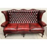 A GOOD QUALITY THREE SEATER WING BACKED LEATHER COUCH, with button back detail and scrolling head an