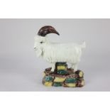 A glazed pottery model of a goat possibly Irish, standing on a base of coloured cobble stones, 18cm