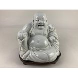 A Chinese pottery seated laughing Buddha on hardwood stand, paper label with character marks, 19cm