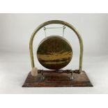 A brass dinner gong on oak base, the support with Greek key design, the mallet with a wooden handle,