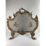 A Rococo style brass fire screen, with winged cherubs mounted on either side of mesh, one using