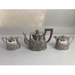 An Asian white metal three piece tea set, with embossed fruiting vine design