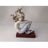 A Lladro porcelain figure of a mermaid holding a shell containing a faux pearl, 17cm high, on a