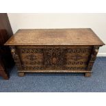 A carved oak coffer, the hinged rectangular top above a two panelled front, flanked by carved