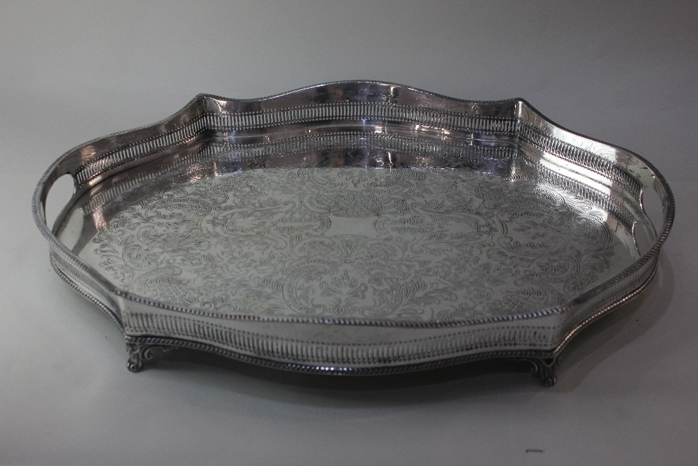 A silver plated serving tray with serpentine shaped pierced raised border and scroll and foliate