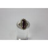 A garnet dress ring the oval cut stone within a cubic zirconia border