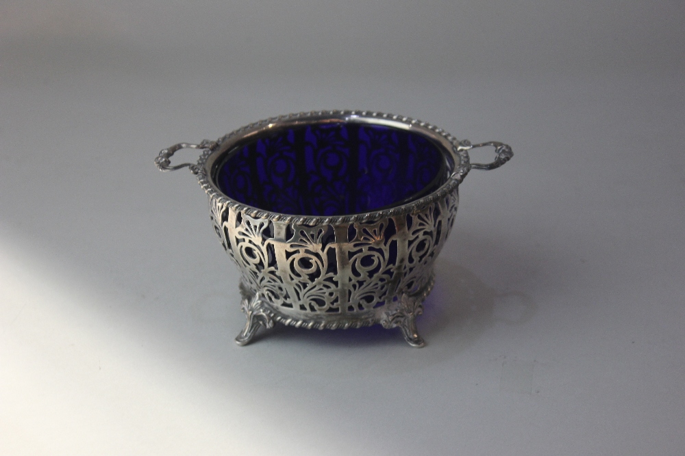 A George VI pierced silver two handled circular dish with blue glass liner on four scroll feet,
